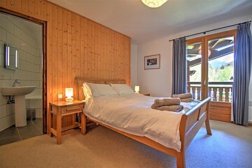 A cozy bedroom with wood paneling, a double bed, balcony doors, and a glimpse into an ensuite bathroom.