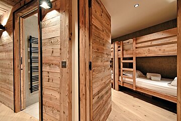 Modern wooden chalet interior with an open bathroom door on the left and a bedroom with built-in wooden bunk beds on the right.