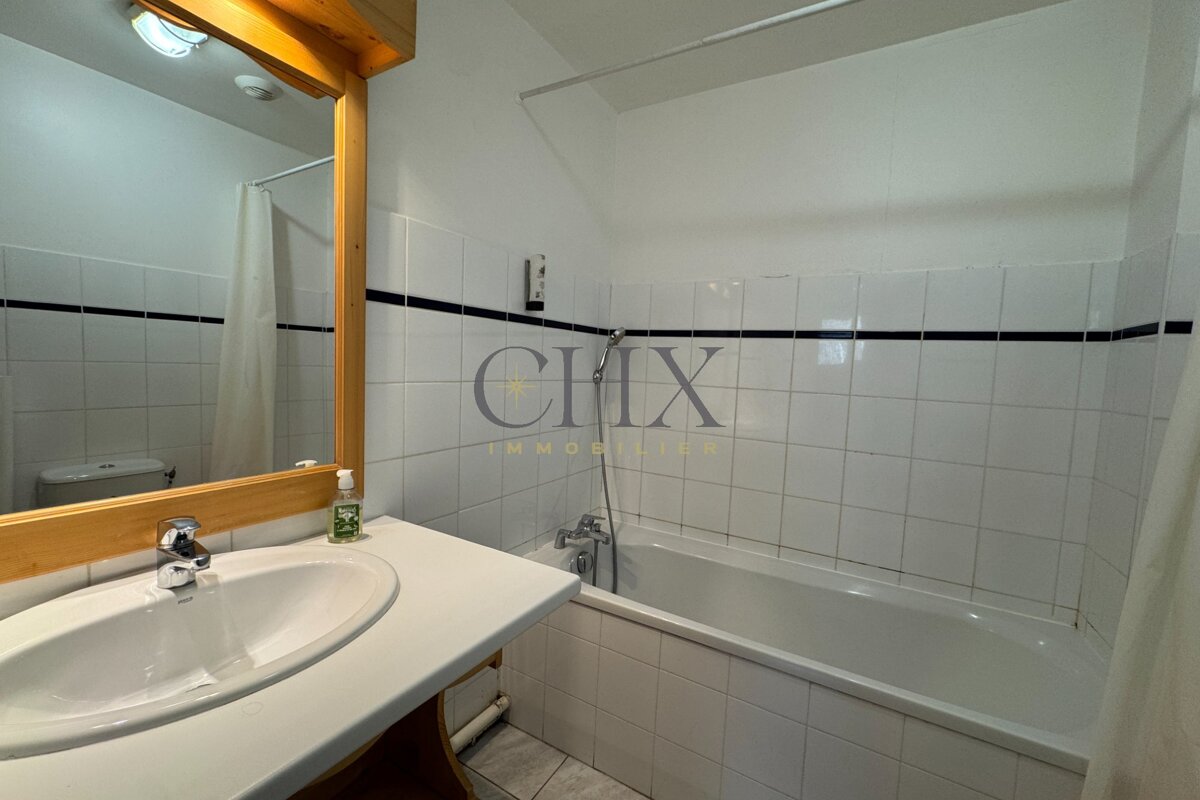 A small tiled bathroom featuring a white sink, a wooden-framed mirror, and a bathtub with a shower attachment.