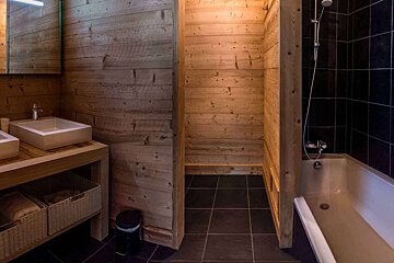 Rustic bathroom featuring light wood-paneled walls, dark tile flooring, a vessel sink vanity, and a bathtub.