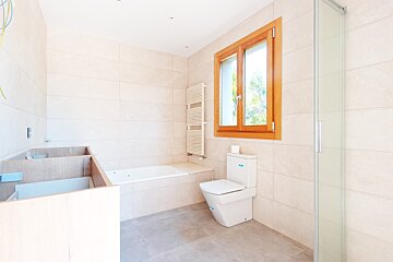 Bright, tiled bathroom in progress with a wooden window, bathtub, toilet, shower, and unfinished vanity cabinets.