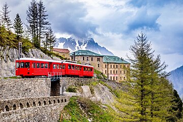 A red train is going down a hill with mountains in the background