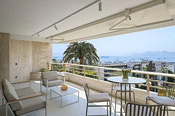 An elegant balcony with modern outdoor furniture offers a scenic view of a coastal city and the ocean beyond.