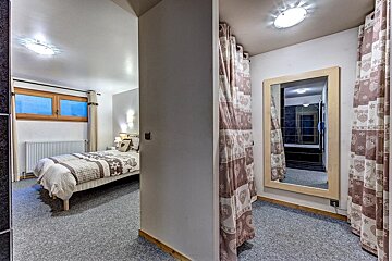 A split view showing a bedroom on the left and a dressing area with a large mirror and patterned curtains on the right.