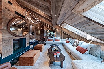 A cozy chalet living room with vaulted wood ceilings, skylights, a large sectional sofa, a fireplace, and warm, rustic-modern decor.