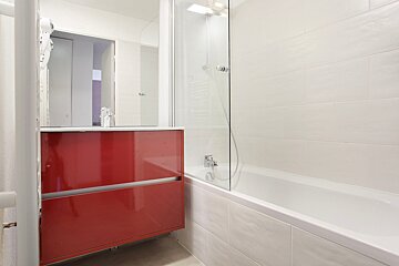 A bathroom with a red cabinet and a white bathtub