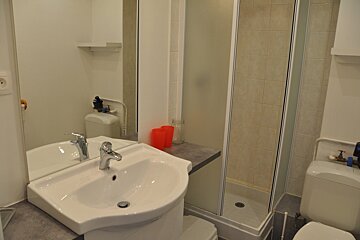 A compact, modern bathroom featuring a white sink with a large mirror, a glass-enclosed shower stall, and a toilet.