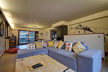 Cozy chalet living room with a grey sofa, wooden table, and ski-themed wall mural. Large window offers outdoor views.