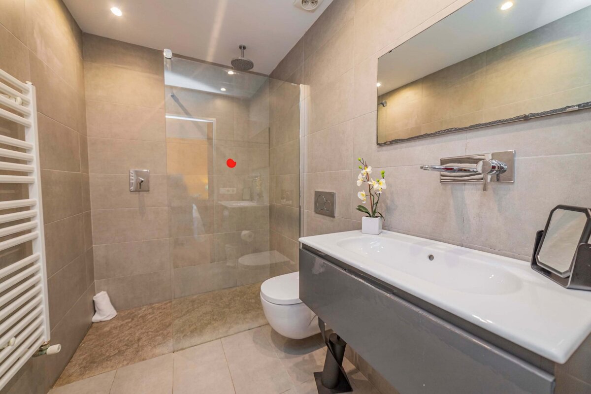 A modern, neutral-toned bathroom featuring a glass shower, wall-mounted toilet, floating vanity, large mirror, and towel warmer.