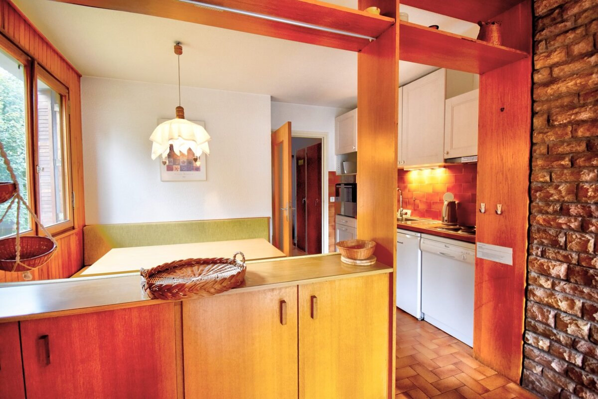 Mid-century modern home interior featuring a cozy dining nook and a kitchen visible through warm wooden cabinetry and a brick wall.