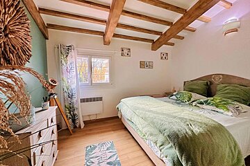 Cozy bedroom featuring wooden ceiling beams, a bed with green botanical bedding, light wood floors, and a dresser.
