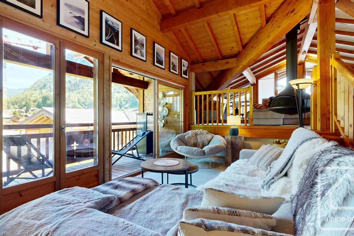 Cozy alpine chalet interior featuring warm wooden beams, plush seating with fur blankets, and large windows offering scenic mountain views.