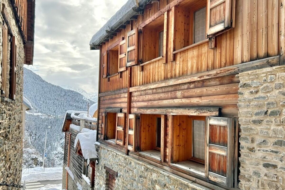 Rustic wooden chalets with stone bases and shutters in a snowy alpine village.