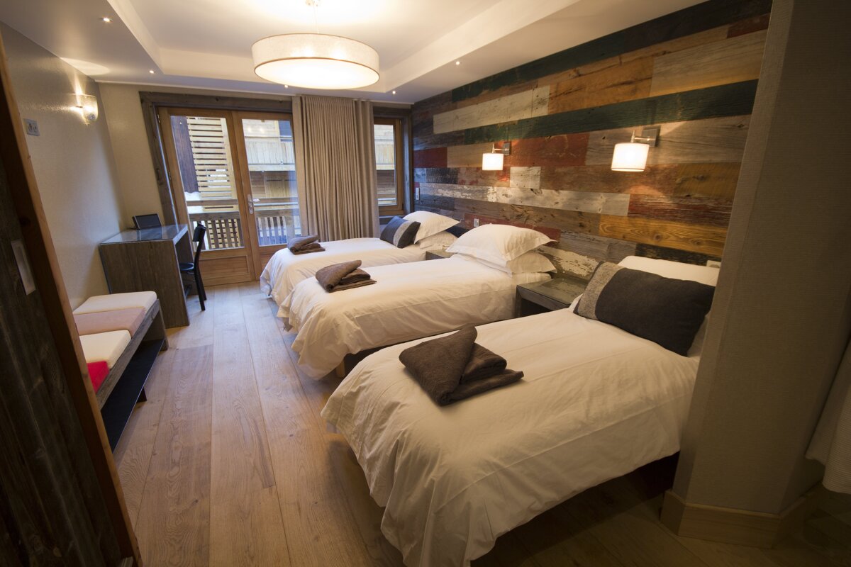 A hotel room with three beds and a wooden wall