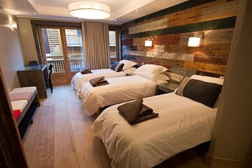 A cozy rustic bedroom featuring three single beds, a colorful wood panel accent wall, and light hardwood floors.