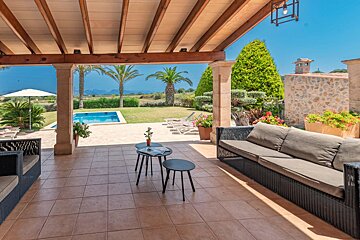 A patio with a couch and two tables with a pool in the background