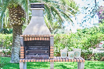A brick barbecue with three pots on a table in front of it
