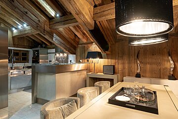 Chic chalet interior combining rustic wood beams/walls with a modern kitchen, elegant dining area, and sophisticated lighting.