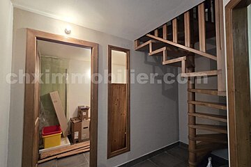 A hallway with a wooden spiral staircase, an open doorway revealing moving boxes, and a narrow wooden panel on neutral walls.