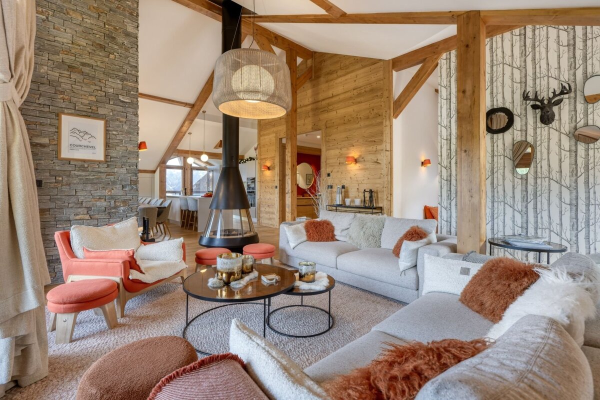A luxurious, spacious chalet living room featuring a suspended fireplace, exposed wood beams, stone wall, and cozy seating in a modern rustic style.
