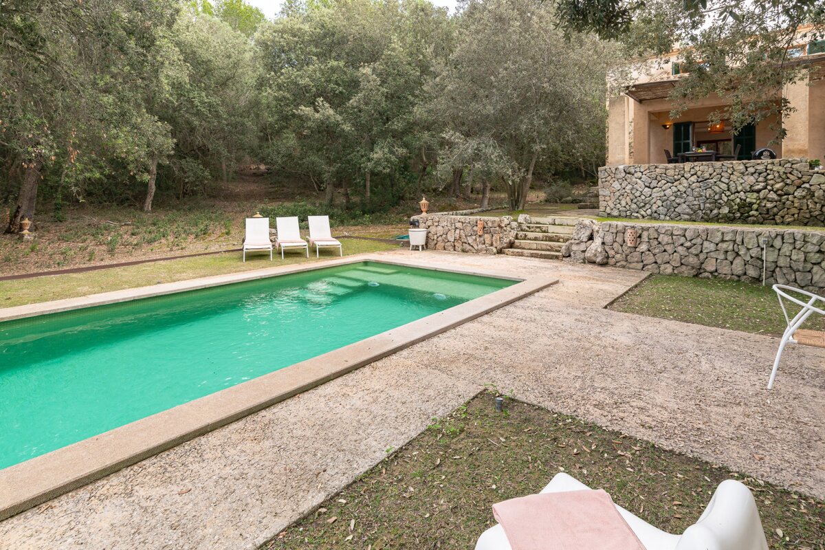 A large swimming pool is surrounded by chairs and a stone wall