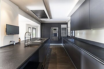 Sleek modern kitchen with dark gray cabinets, black countertops, built-in appliances, and a large island with a sink.