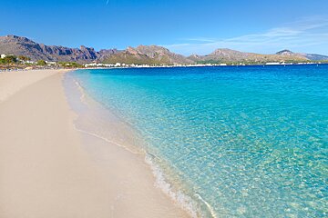 A beach with clear water and mountains in the background