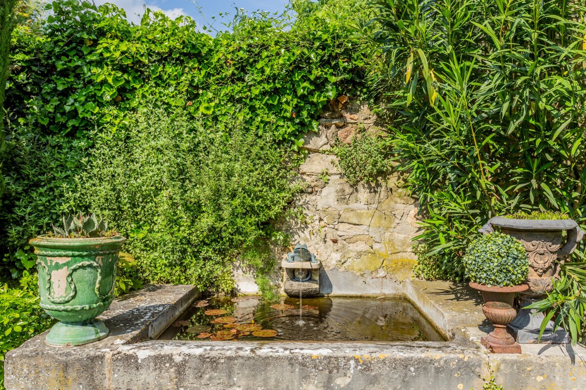 A fountain in a garden surrounded by potted plants