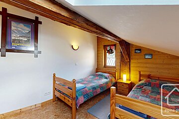 A cozy, rustic attic bedroom with two single beds, wood paneling, exposed beams, a sloped ceiling, and a mountain poster on the white wall.