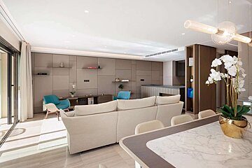 Spacious, modern open-plan living room with a beige sofa, blue accent chairs, a dining table, and a white orchid. Sleek paneled walls and natural light.