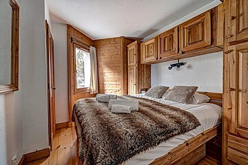 Rustic wooden bedroom with a cozy bed, furry blanket, built-in cabinets, and a bright window.