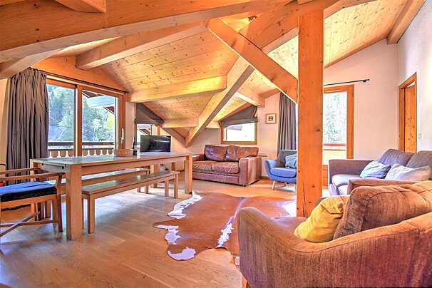 Cozy alpine cabin living room with exposed wooden beams, a dining table, leather and fabric sofas, and a cowhide rug.