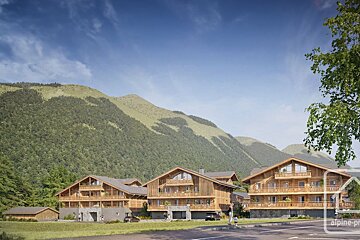 Modern wooden chalets with balconies are nestled against a lush green mountain range under a clear blue sky, depicting an alpine resort.