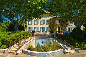 A large house with blue shutters and a pond in front of it