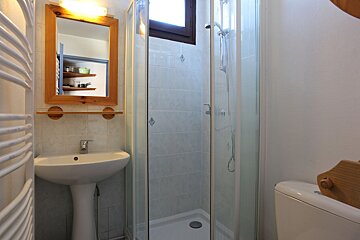 A small, functional bathroom featuring a pedestal sink, wooden-framed mirror, and a glass-enclosed shower, with a toilet partially visible.