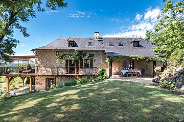A large stone house with a large deck and a table and chairs on it