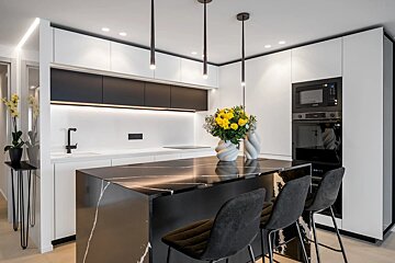 Modern kitchen with a black marble island, white cabinets, black accents, pendant lights, and vibrant yellow flowers.