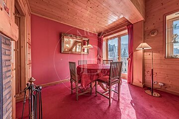 A wooden-paneled room with red walls and carpet, featuring a dining table set, a large mirror, and a window with curtains.