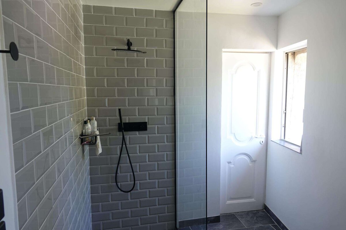 A bathroom with grey tiles and a black shower head
