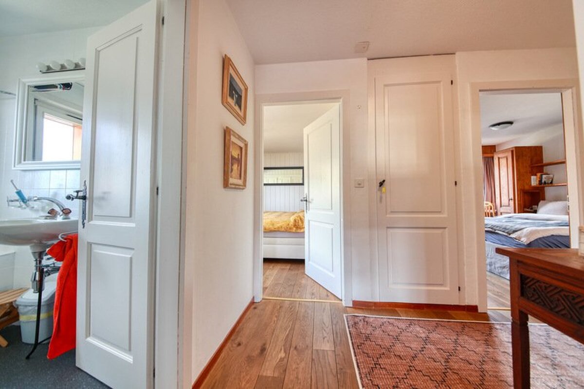 A bright hallway with wooden flooring and white doors leading to a bathroom and bedrooms.