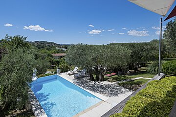 A large swimming pool is surrounded by trees and bushes