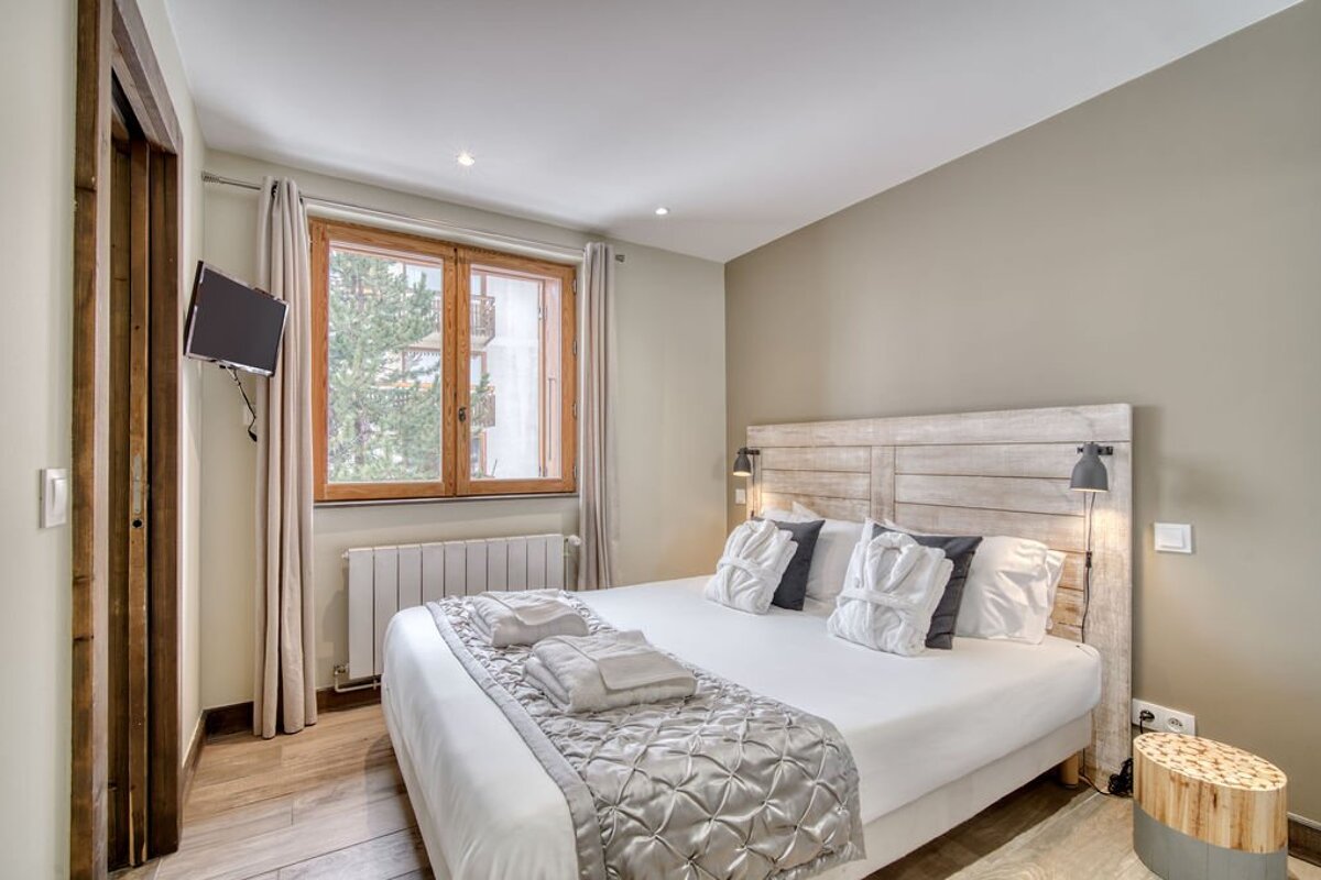 A cozy bedroom featuring a double bed with a light wood headboard, neutral walls, and a window.