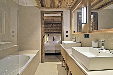 A modern rustic bathroom featuring a double vanity, bathtub, and an open doorway leading to a cozy bedroom.