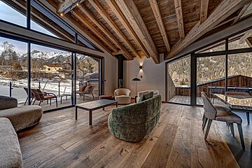 A modern chalet's cozy interior with exposed wooden beams, large windows offering snowy mountain views, and contemporary furniture in a winter setting.
