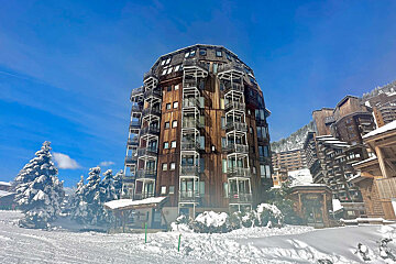 A large wooden building with many balconies is surrounded by snow