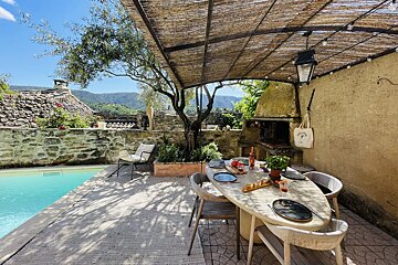 A patio with a table and chairs under a canopy overlooking a pool