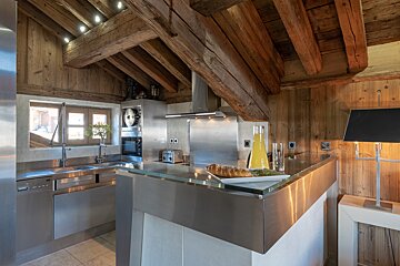 A chic stainless steel kitchen with rustic wooden walls and exposed beams under an angled ceiling. Bread and juice are on the counter.