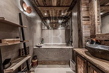 A rustic bathroom with concrete and wood finishes, featuring a large built-in tub, stone vessel sink, and wood-paneled ceiling.