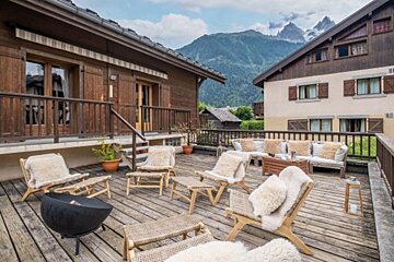 A wooden deck with chairs and a fire pit with mountains in the background