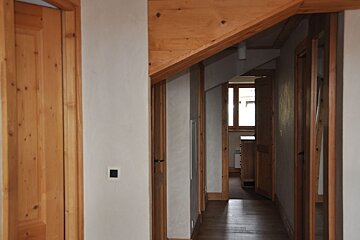 Rustic hallway with wooden doors, a slanted wooden ceiling, and light walls leading to a windowed room.